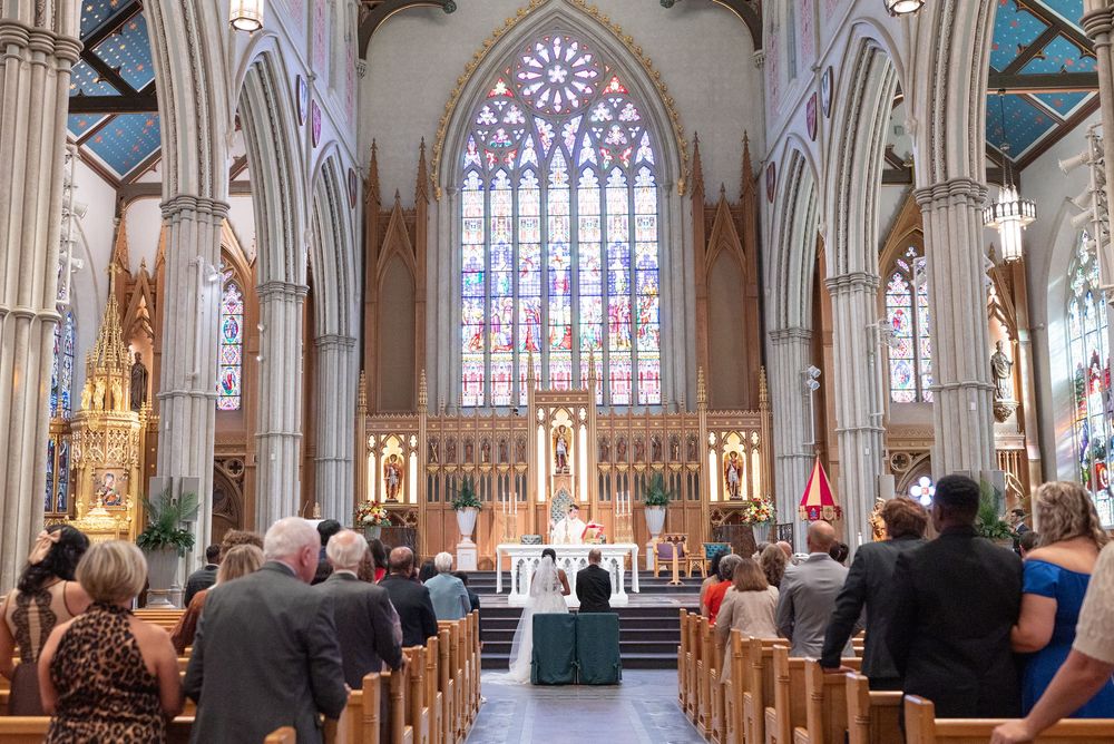 Guests seated in ornate Gothic church pews during a wedding ceremony with stained glass windows and grand altar.
