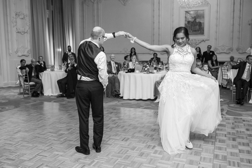Black and white photo of bride and groom sharing their first dance at elegant wedding reception ballroom.