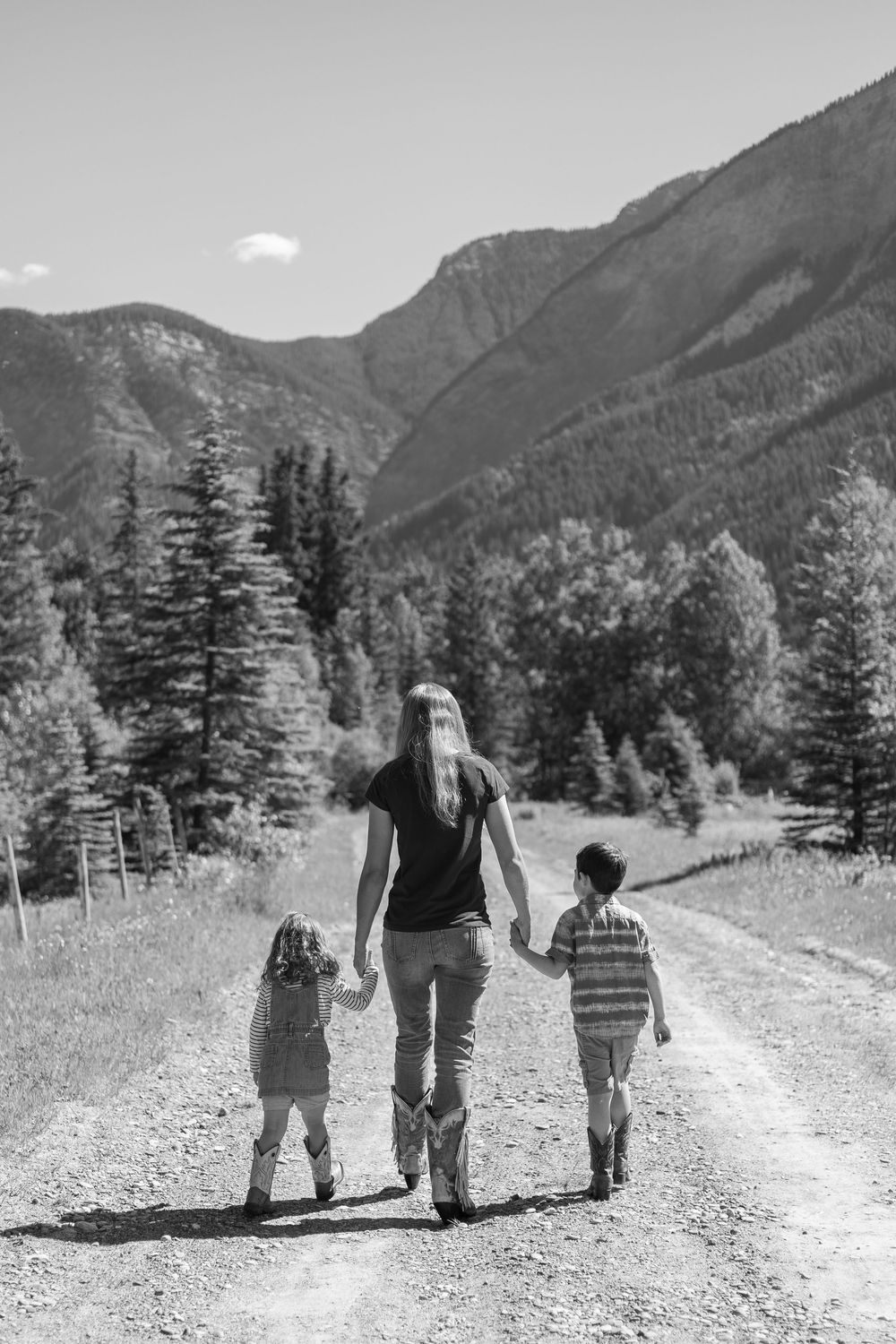 Black and white photo of a mother walking with two children on a mountain dirt road surrounded by trees.