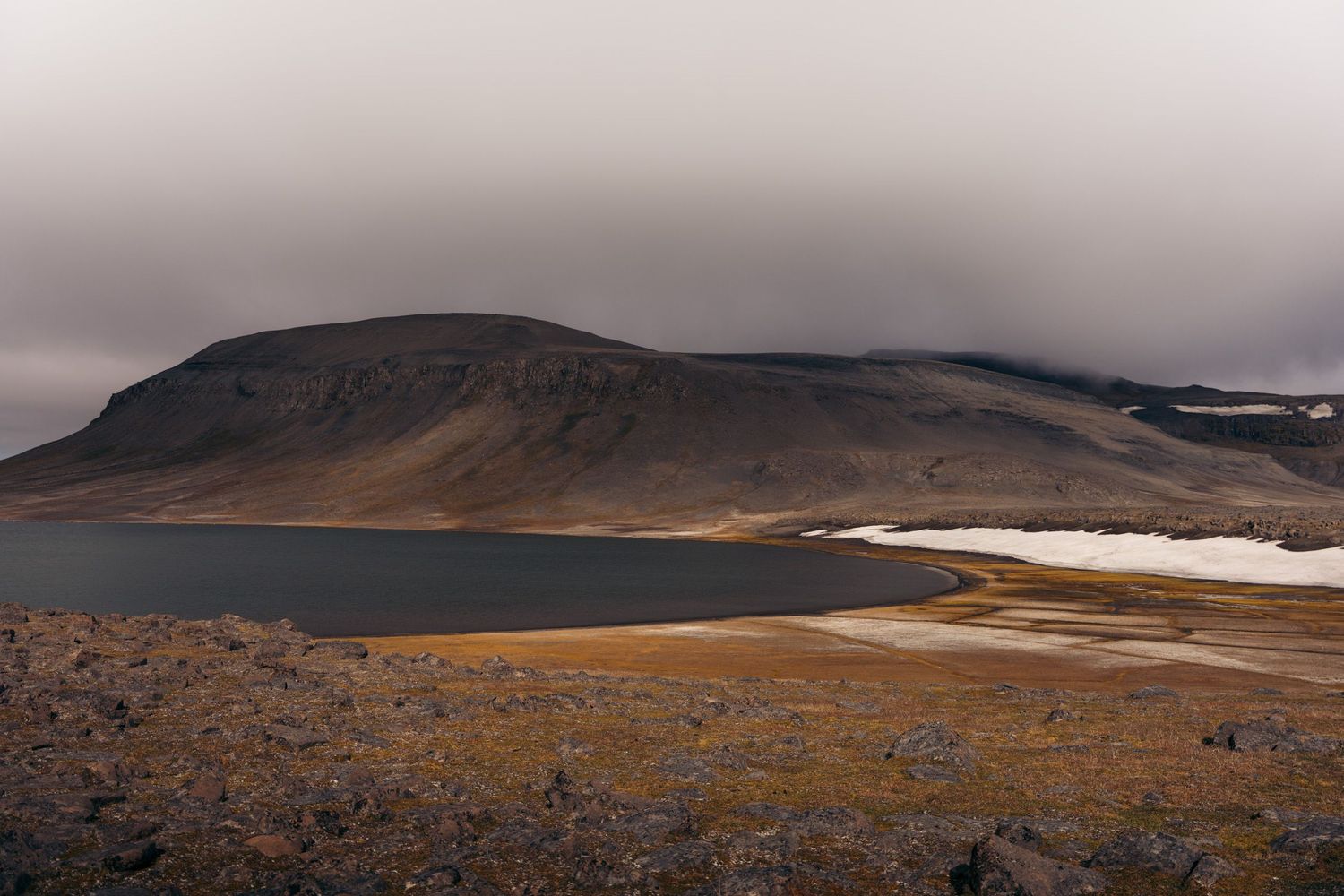Lac et montagne tabulaire de Sundneset sous un ciel bas, névé blanc à droite