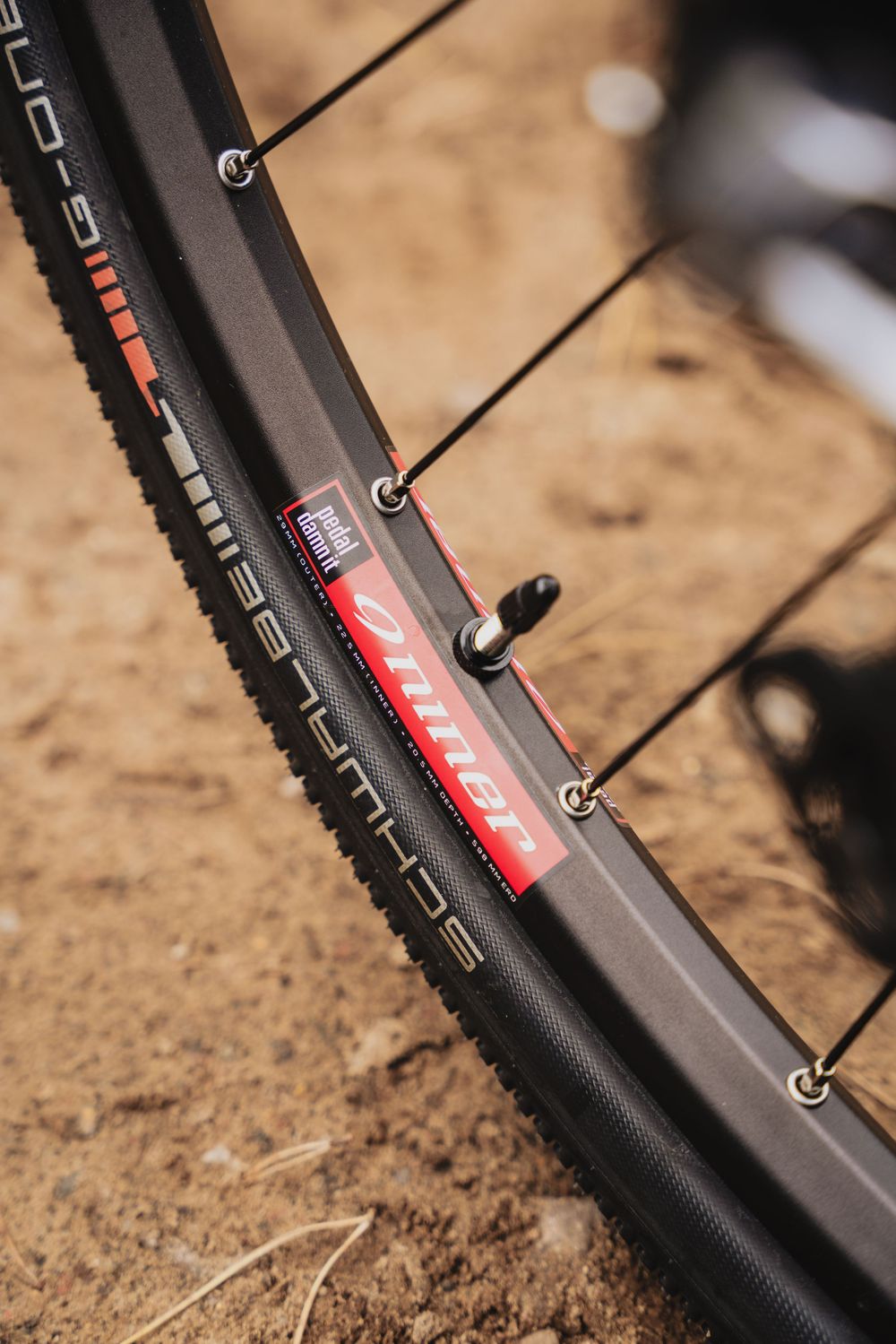 Close-up of a mountain bike wheel with knobby tire, carbon rim, and red Bullet valve stem on dirt ground.