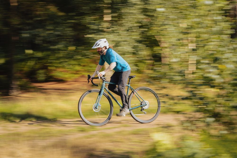 Cyclist in teal jersey and white helmet rides a road bike through a forest trail with motion blur background.