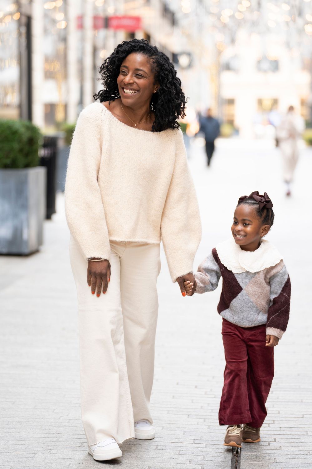 Smiling Black mom and young daughter holding hands while strolling along a decorated urban walkway.