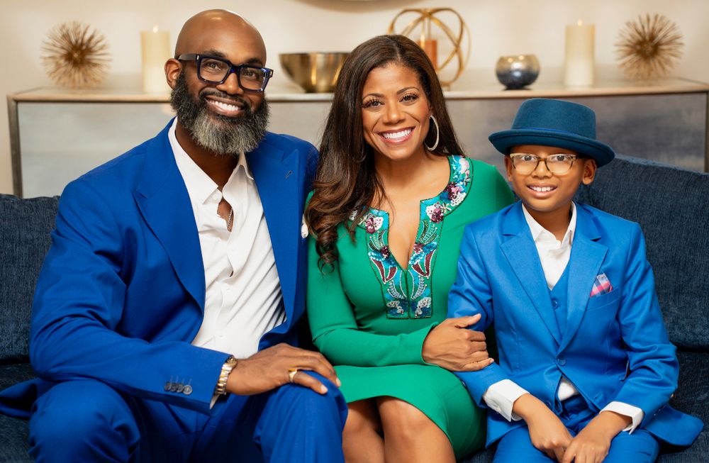 Happy Black family of three in coordinating blue and green outfits sitting together on a sofa.