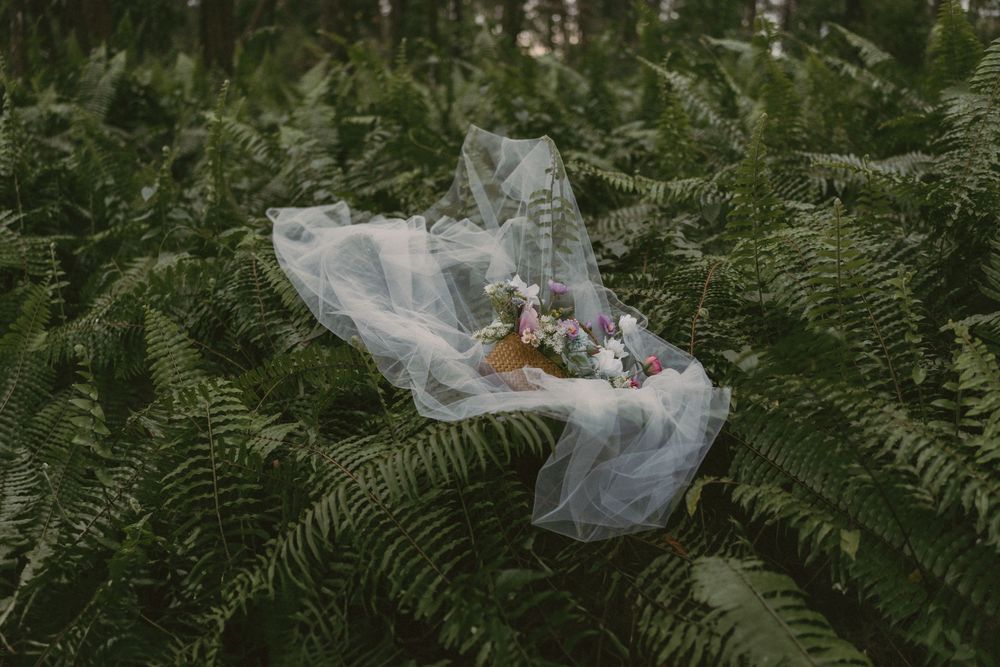 Bridal veil and floral bouquet resting among lush green ferns in a forest setting.