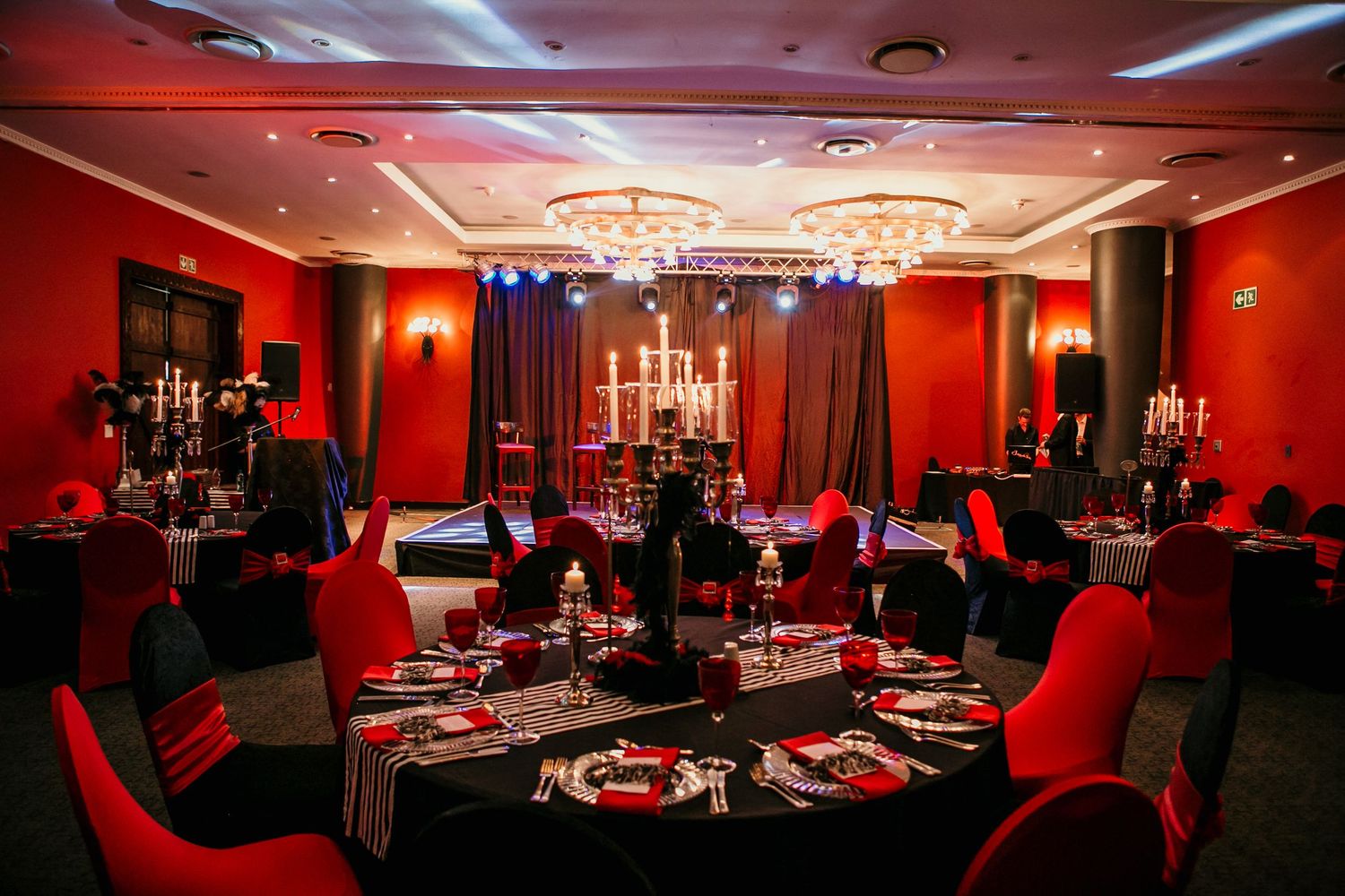 Elegant red and black banquet hall with candelabras, draped tables, and chandelier lighting for a formal event.