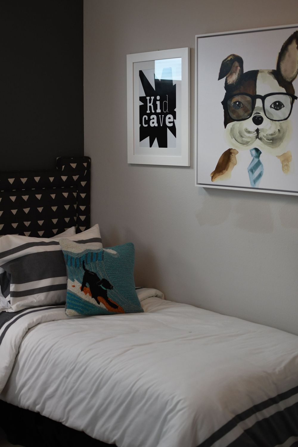 Boys bedroom with dog art, Kid Cave print, striped bedding, teal surfer pillow, and black triangle headboard.