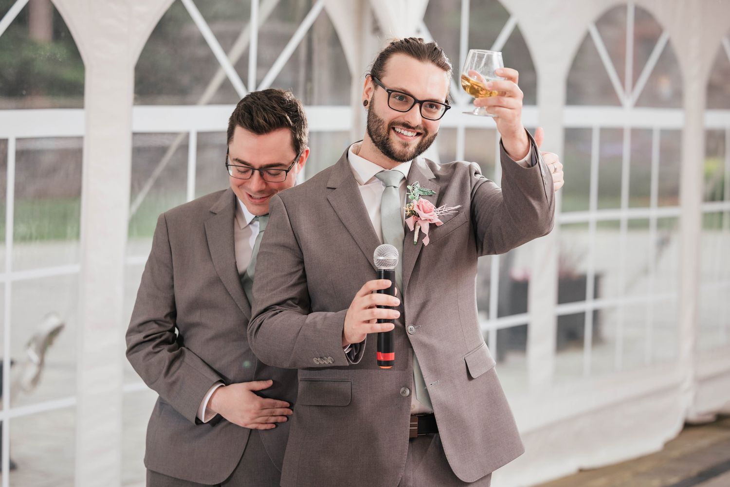 Groomsman raising his glass in a toast, a second groomsman laughing beside him.