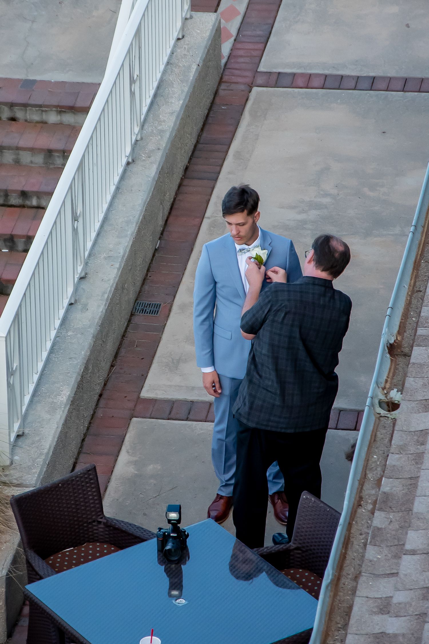 Aerial view of a groom in a light blue suit getting his boutonniere pinned on a rooftop venue.