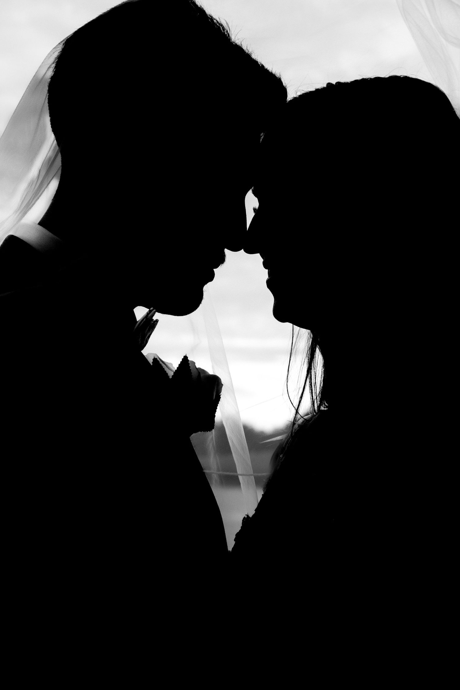 Black and white silhouette of a bride and groom facing each other, foreheads touching romantically.