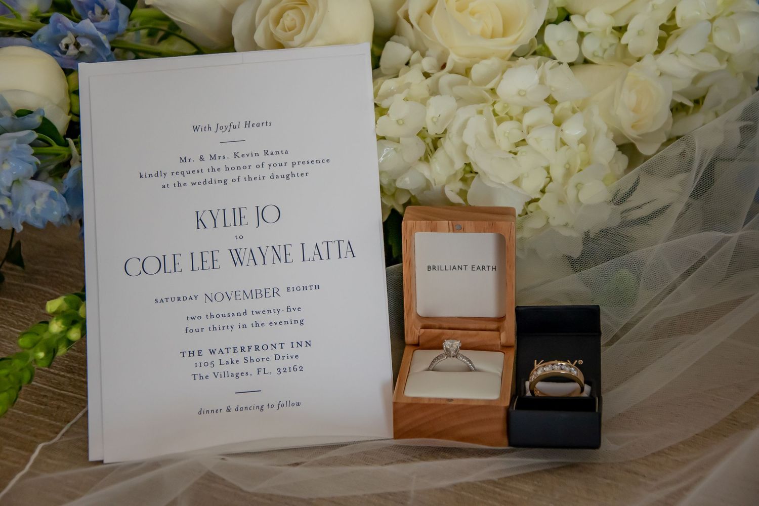 Wedding invitation for Kylie Jo and Cole Lee Wayne Latta displayed with diamond engagement ring and gold wedding band in boxes.