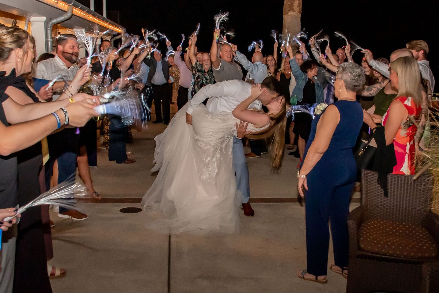 Groom lifts bride in a joyful kiss as wedding guests celebrate with streamers during the grand exit.