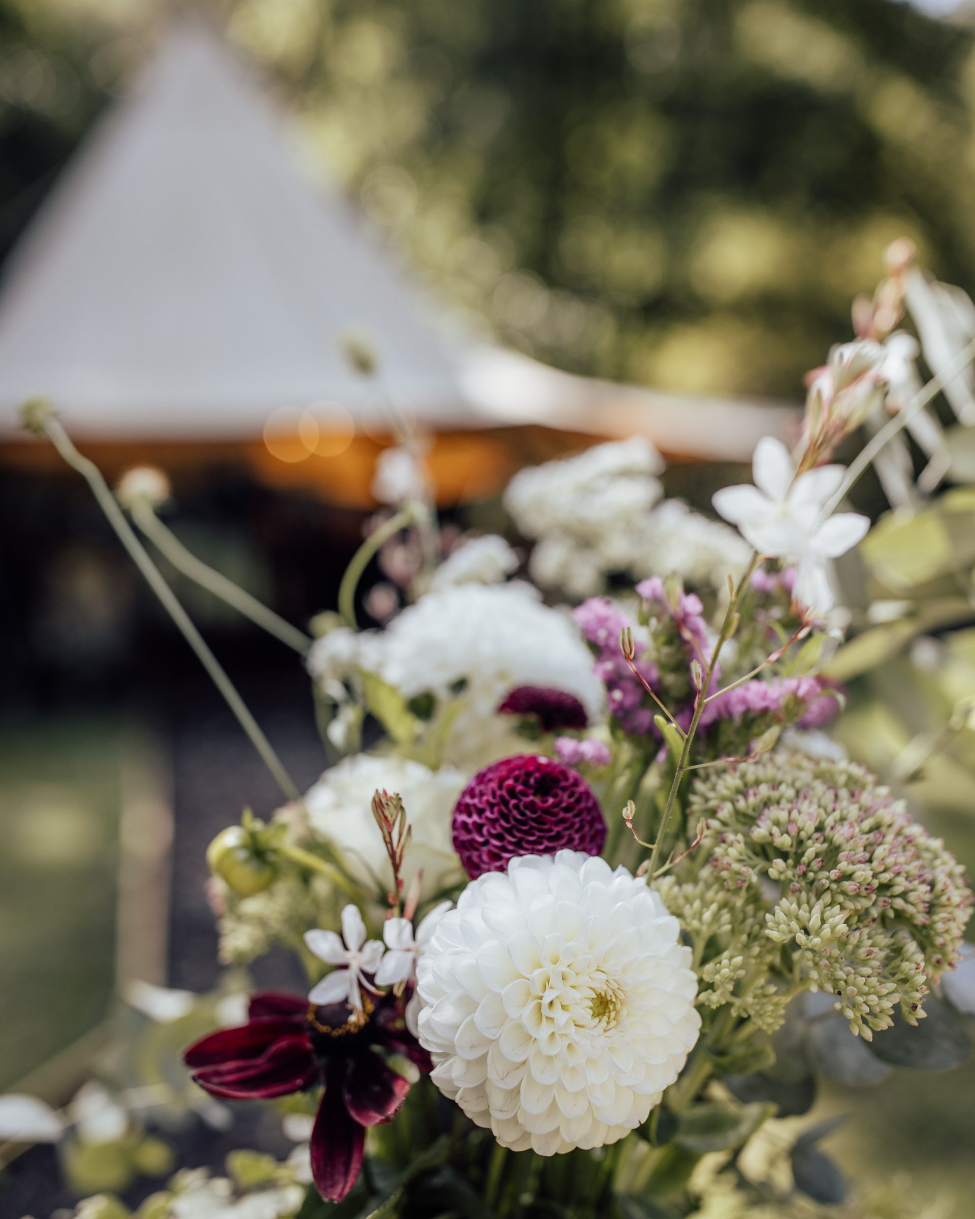 Elegant floral arrangement featuring white and burgundy dahlias with wildflowers at outdoor wedding.