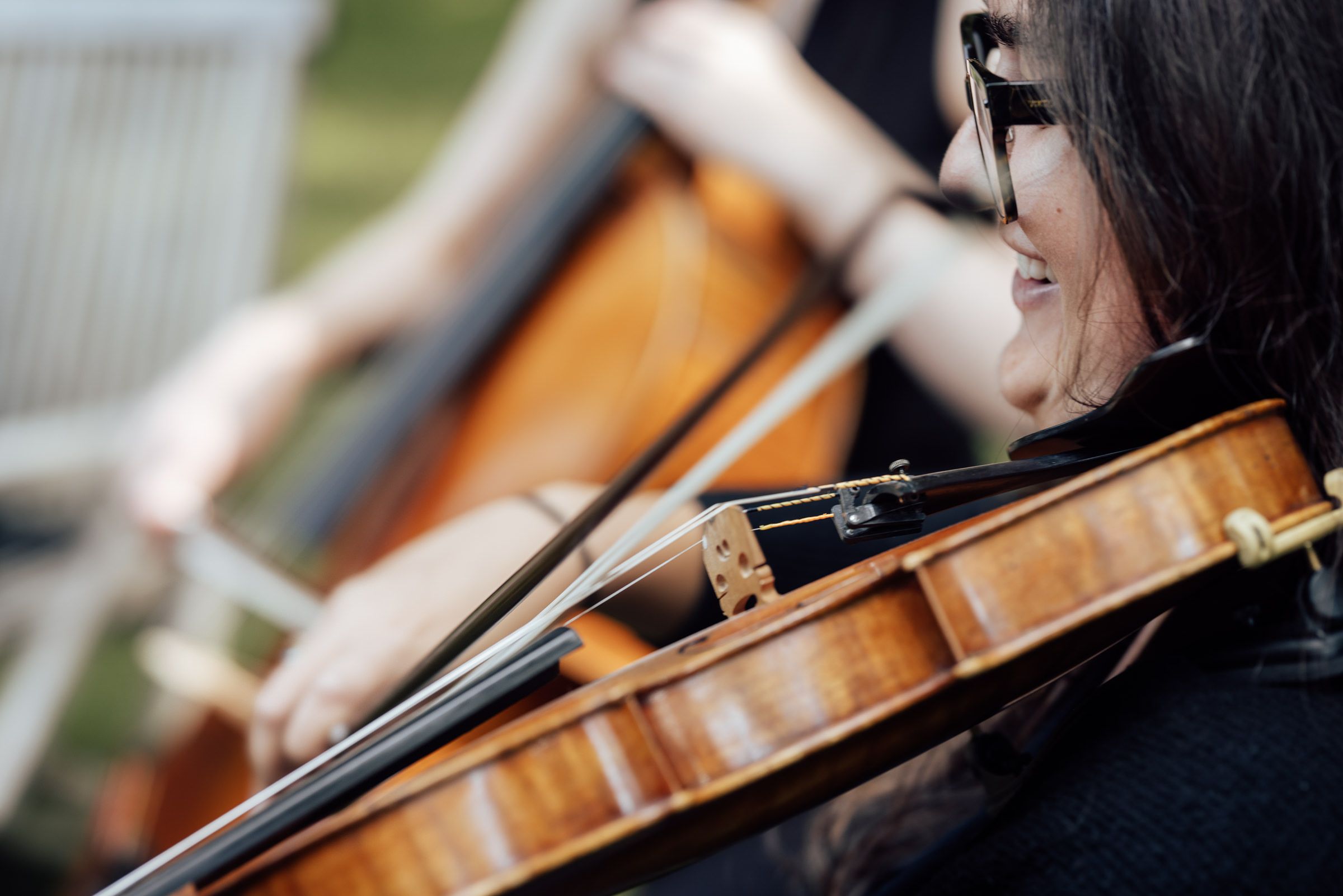 Close-up of a smiling female violinist playing violin outdoors during an orchestra performance.