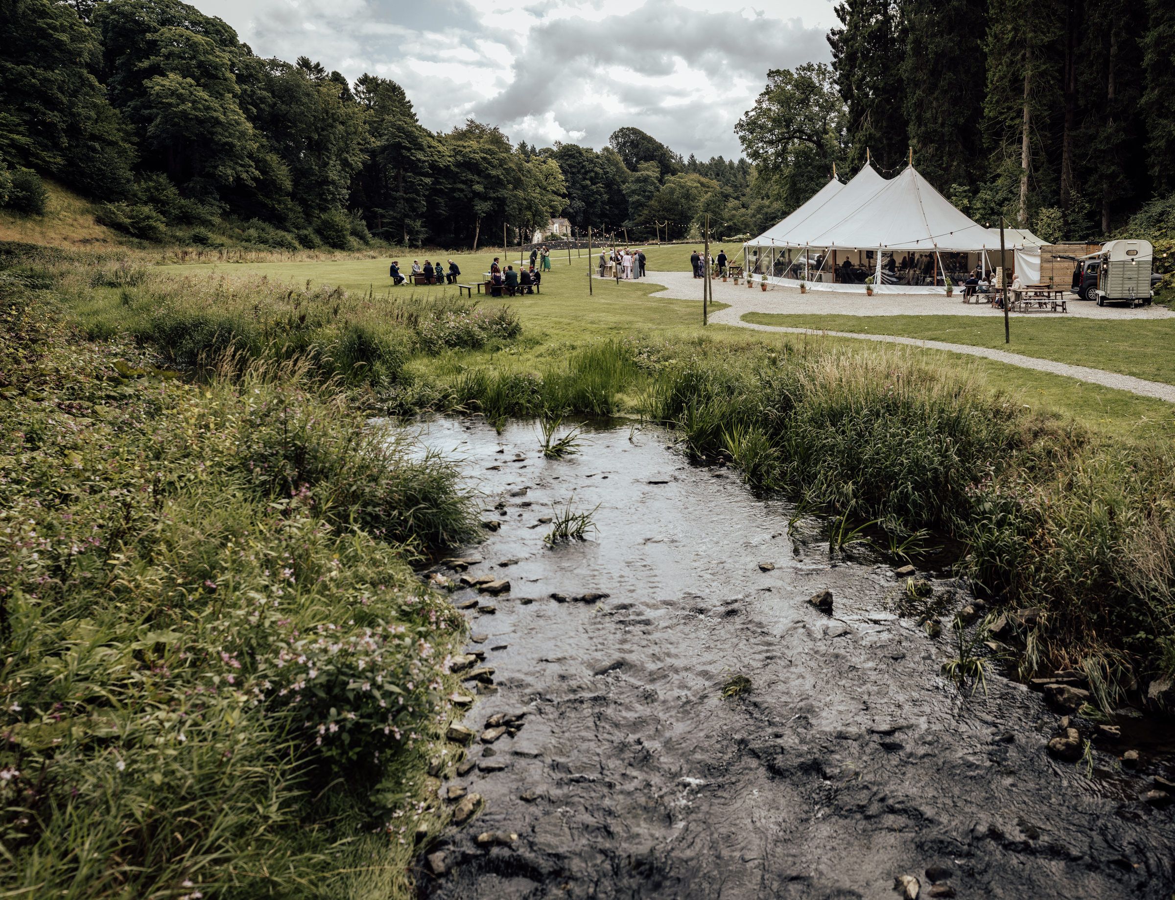 Outdoor wedding marquee tent in lush green countryside with a muddy stream in the foreground.