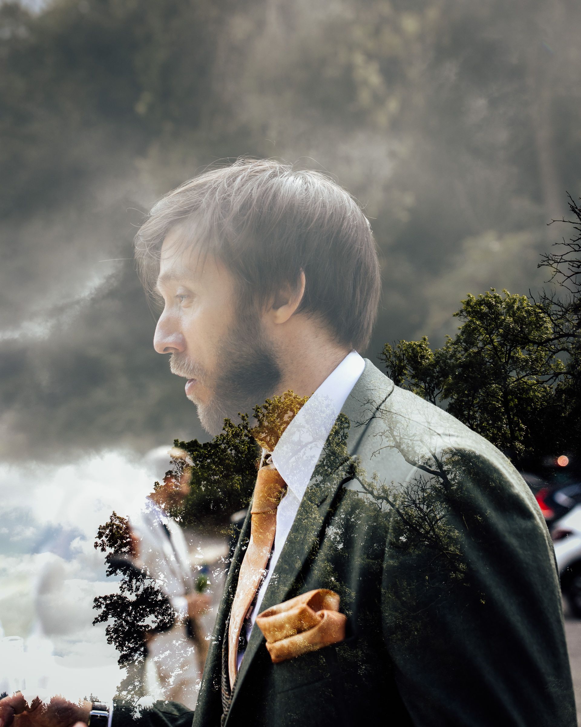 Man in suit and tie with double exposure nature background featuring trees and clouds.
