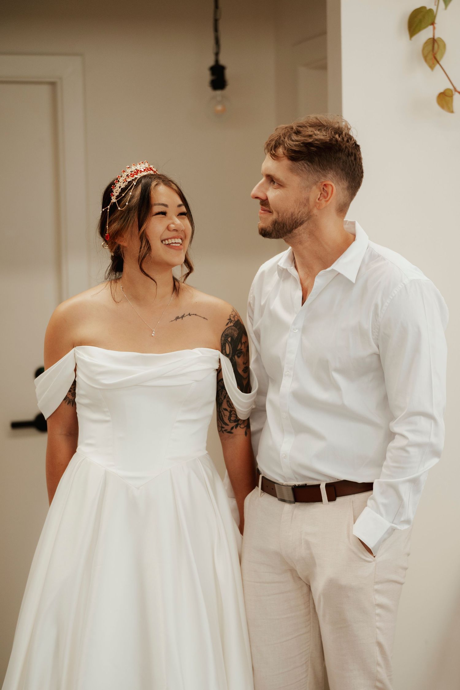 Bride in off-shoulder white gown and groom in white shirt share a joyful moment at their wedding.