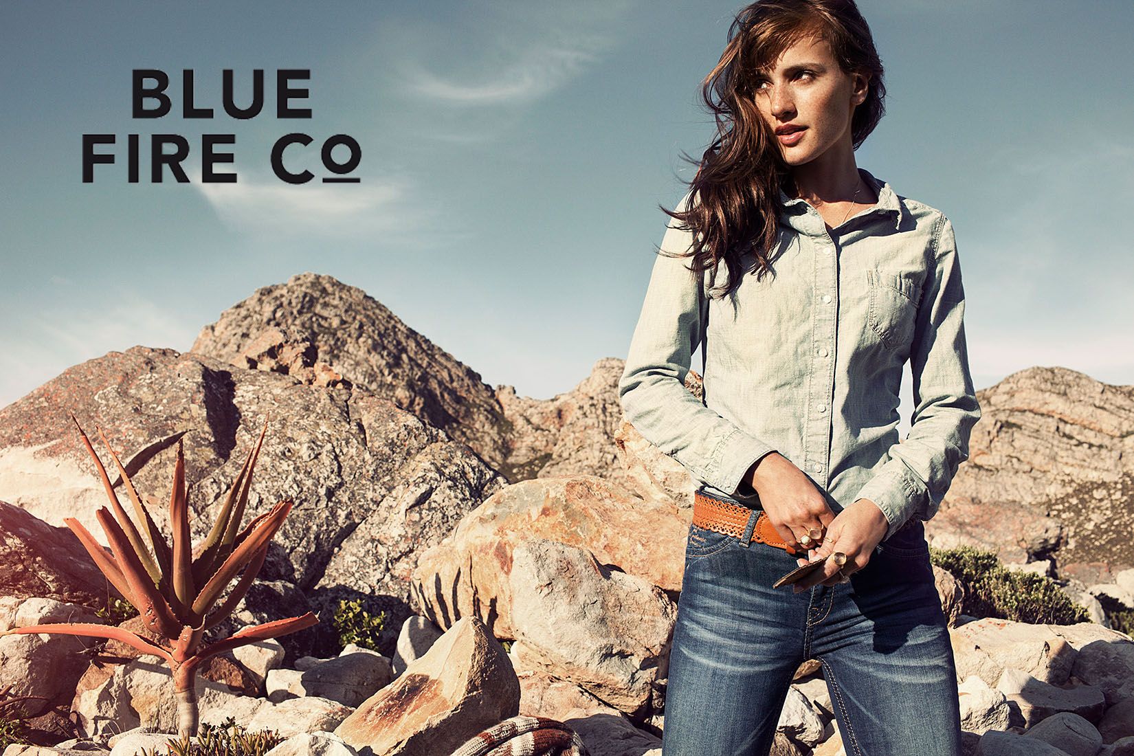 Woman modeling denim shirt and jeans for Blue Fire Co brand in rocky desert landscape setting.