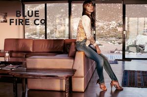 Woman in Blue Fire Co jeans sitting on sofa with snowy mountain view background.