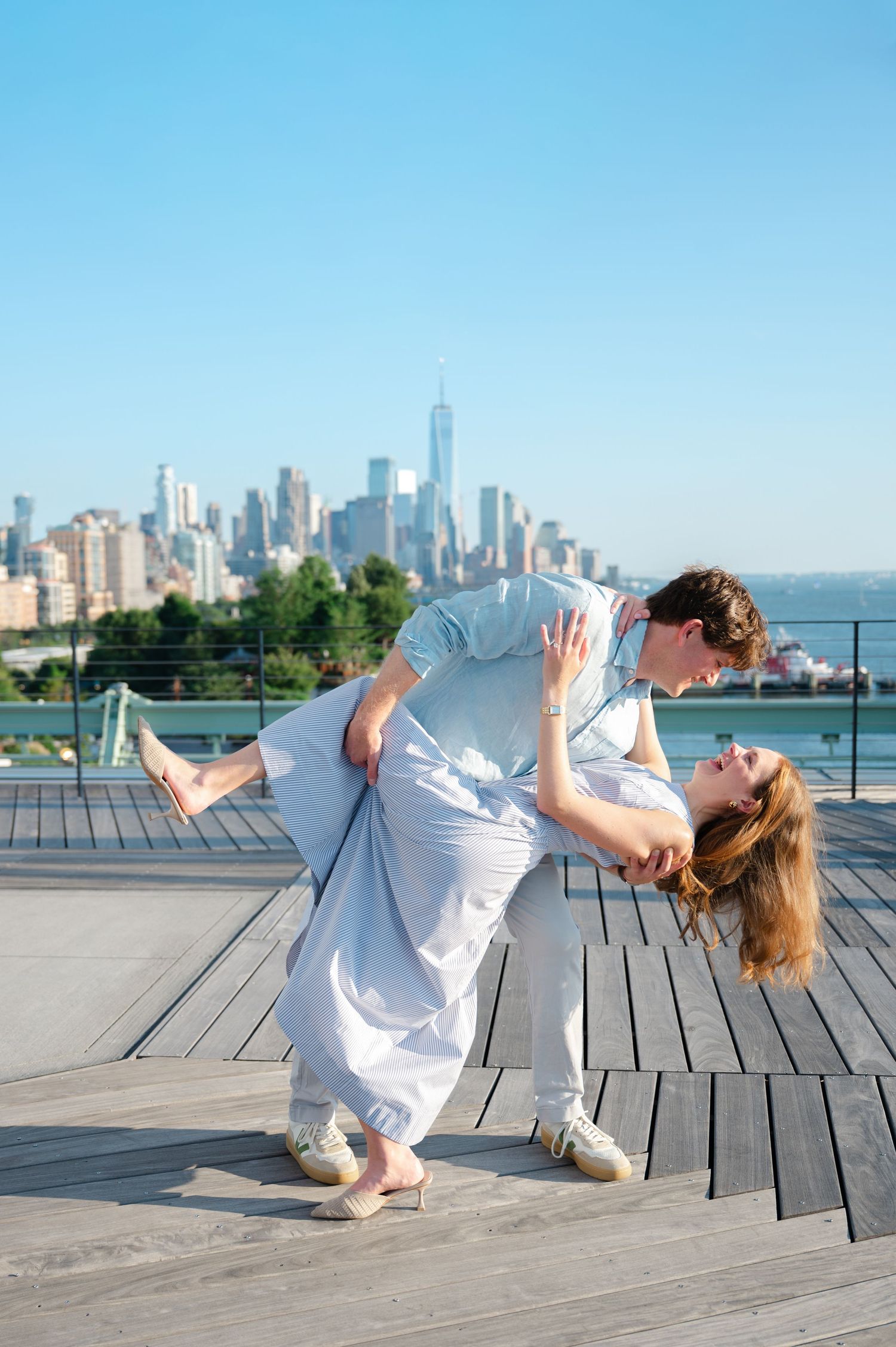 Couple dancing a romantic dip on a wooden deck with the New York City skyline in the background on the rooftop of Pier 57.