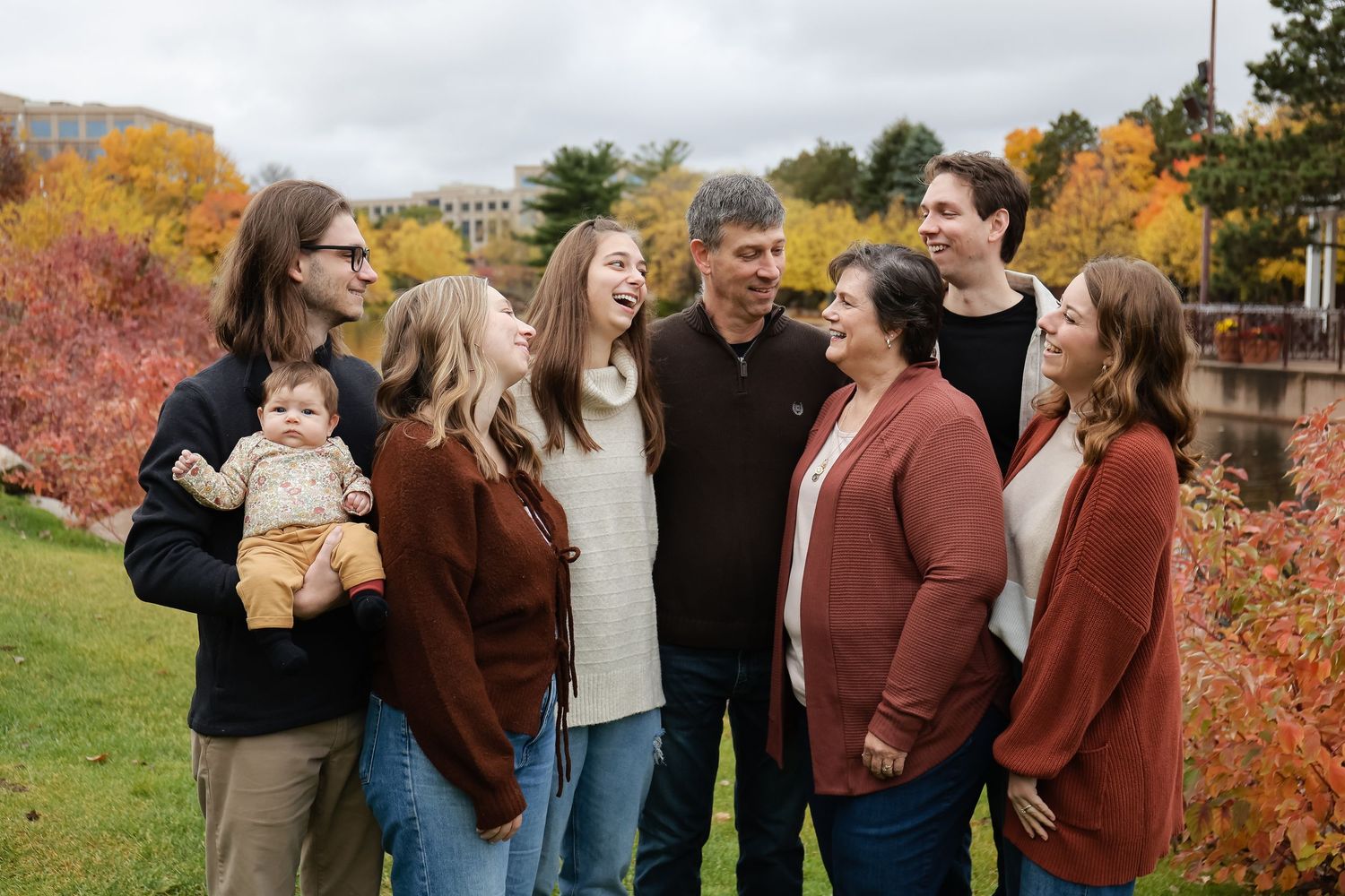 Large multigenerational family group smiling together outdoors surrounded by vibrant fall foliage.