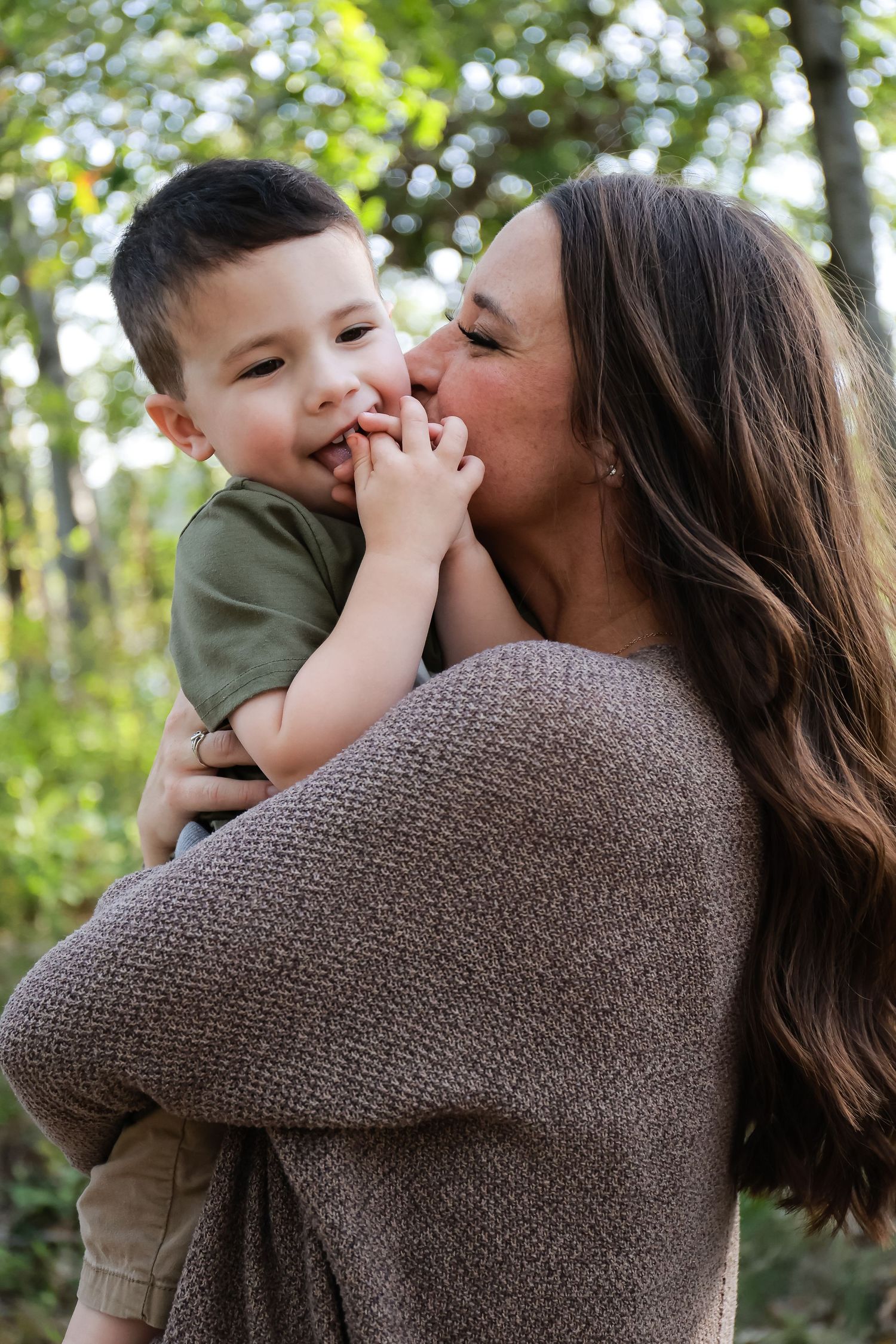 A loving mother kisses her young son on the cheek while holding him outdoors.