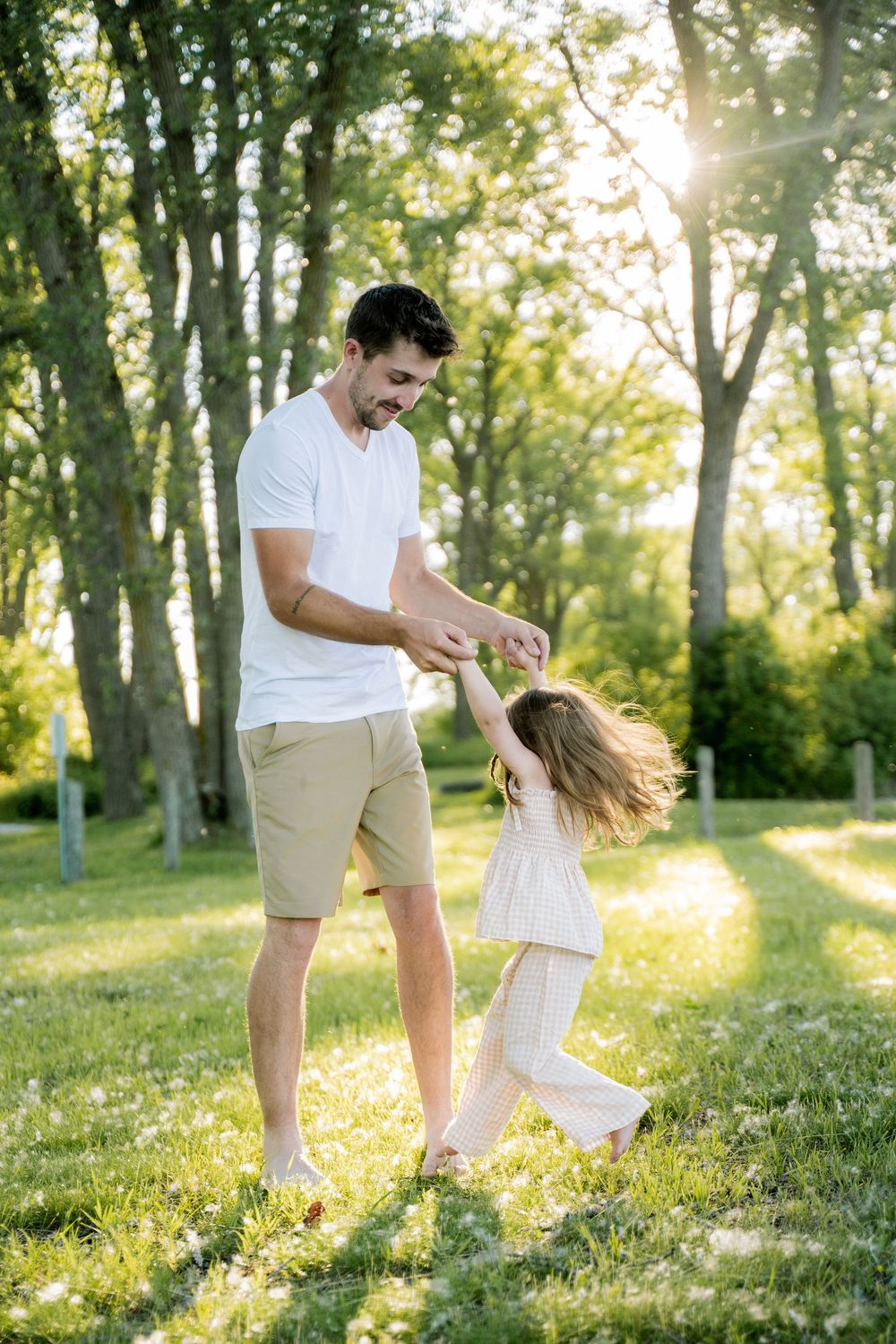 Father and daughter dancing together in a sunny green park, holding hands and spinning joyfully.
