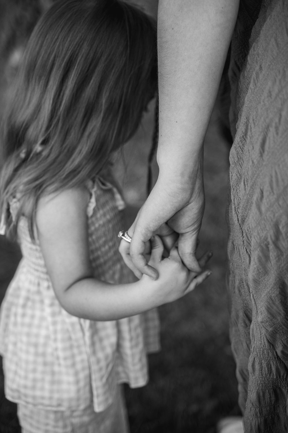 Black and white photo of a young girl holding hands with her mother outdoors.