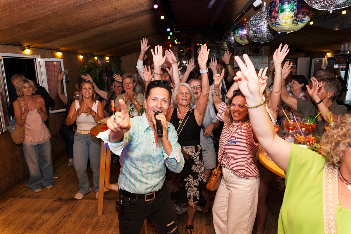 Energetic performer singing into microphone with crowd of excited people raising hands at lively indoor party event.