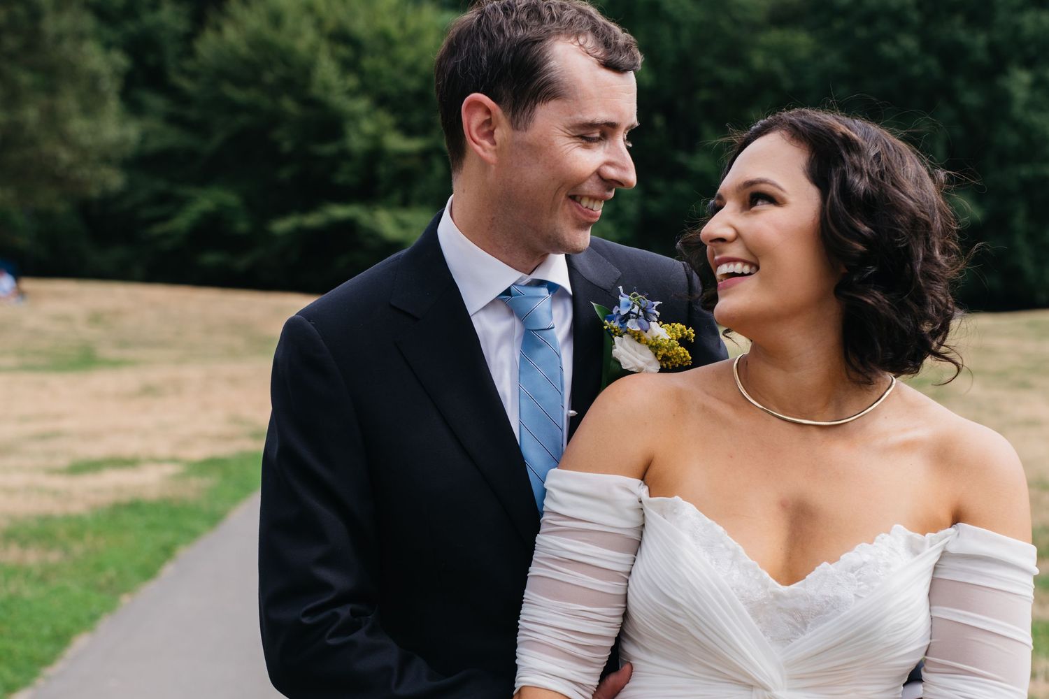 A candid wedding photo of a couple laughing together on a path outdoors.