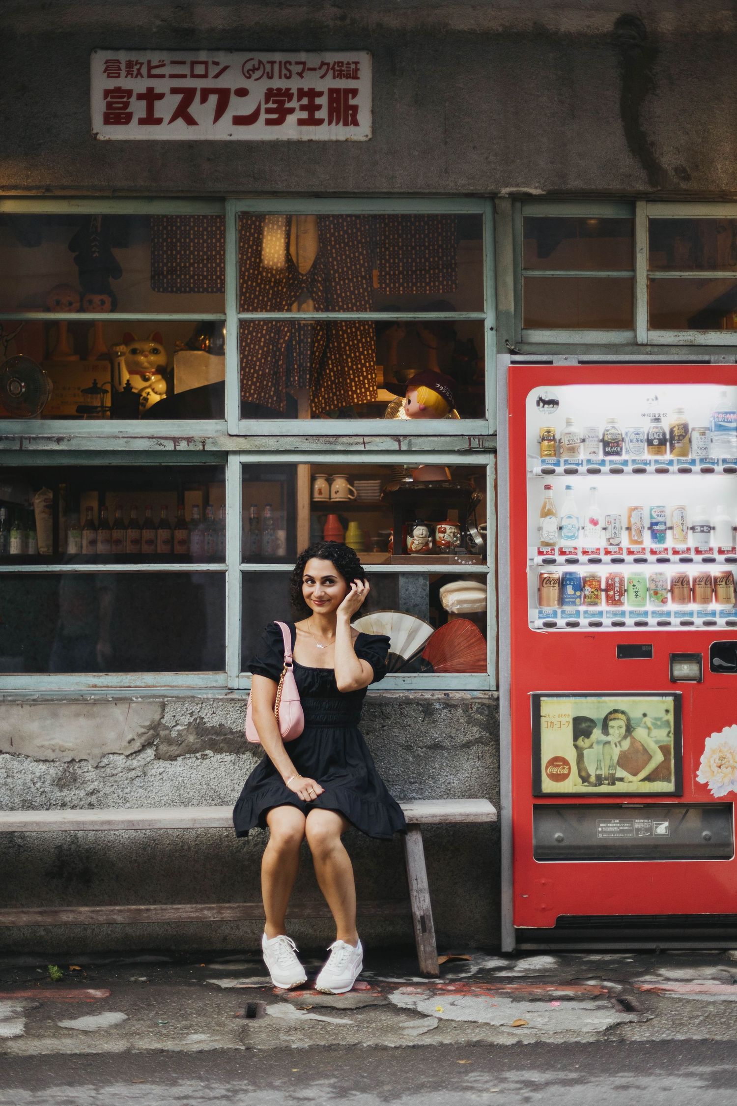 Woman in black dress sitting outside a Japanese shop next to a red vending machine in Japan.