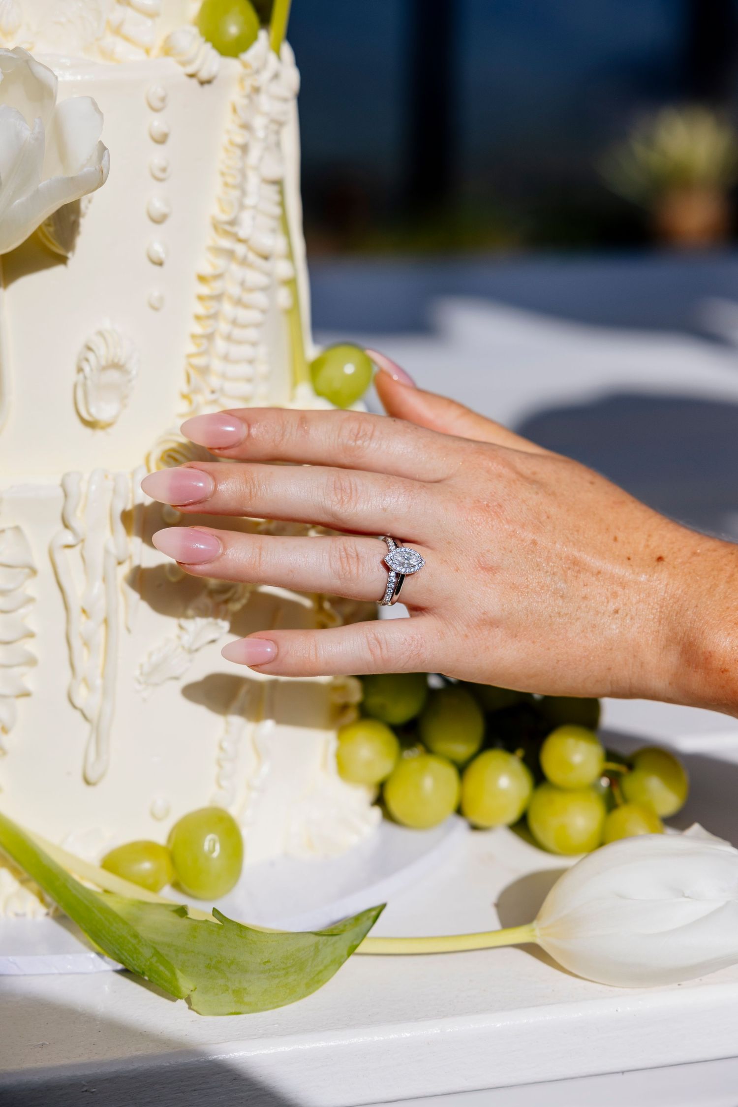 Bride's hand with diamond engagement ring resting on white wedding cake decorated with green grapes product photos queensland