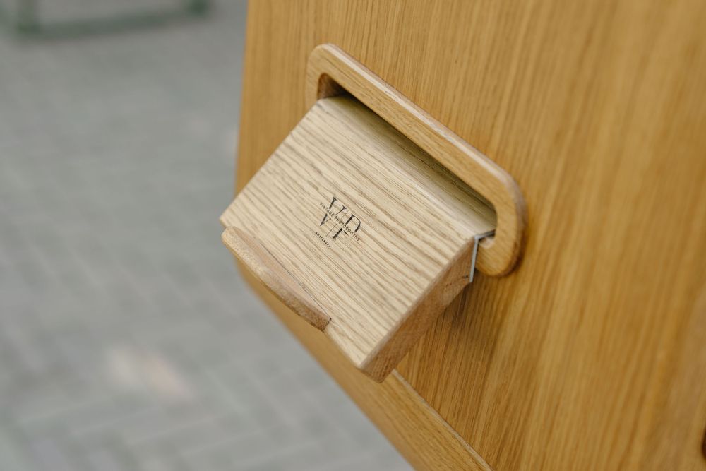 Close-up of a wooden drawer handle with engraved initials on a light oak furniture piece.