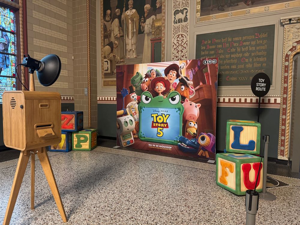 Toy Story 5 movie poster display with vintage camera prop and colorful alphabet blocks in a decorated hall.