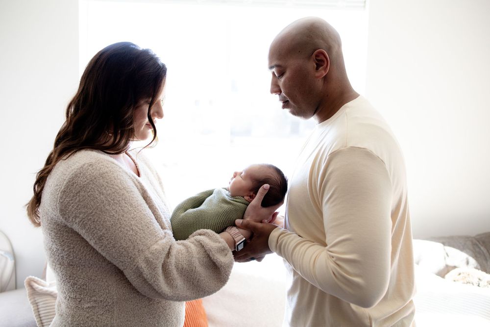 A mother and father stand facing each other in bright room during a newborn lifestyle session in Oak Ridge, TN with Nina Thomas Photography.