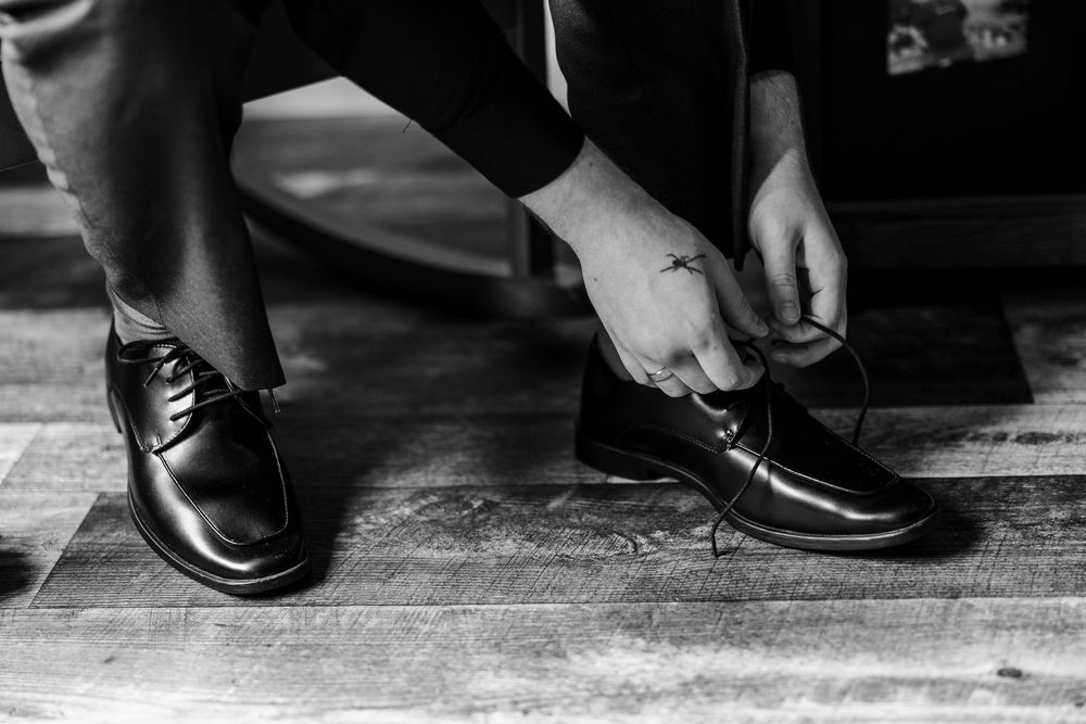 Man tying laces on black dress shoes in black and white photo, formal menswear style.
