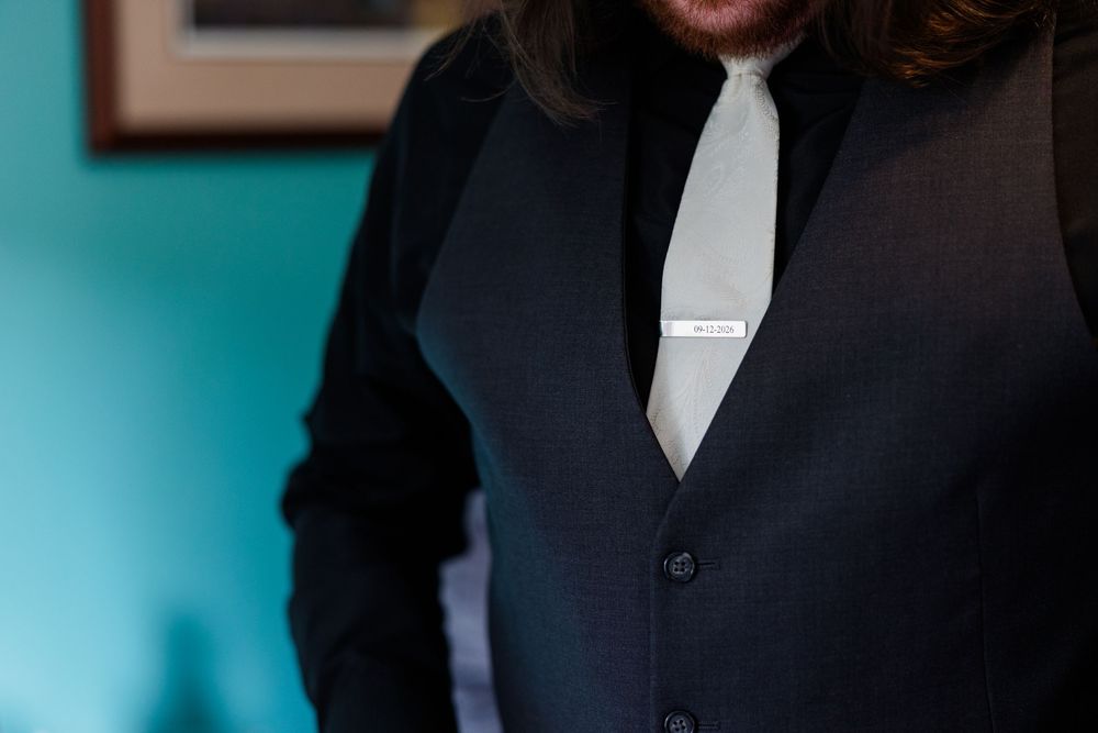 Man in dark suit vest and white tie with silver tie bar, elegant formal wedding attire close-up.