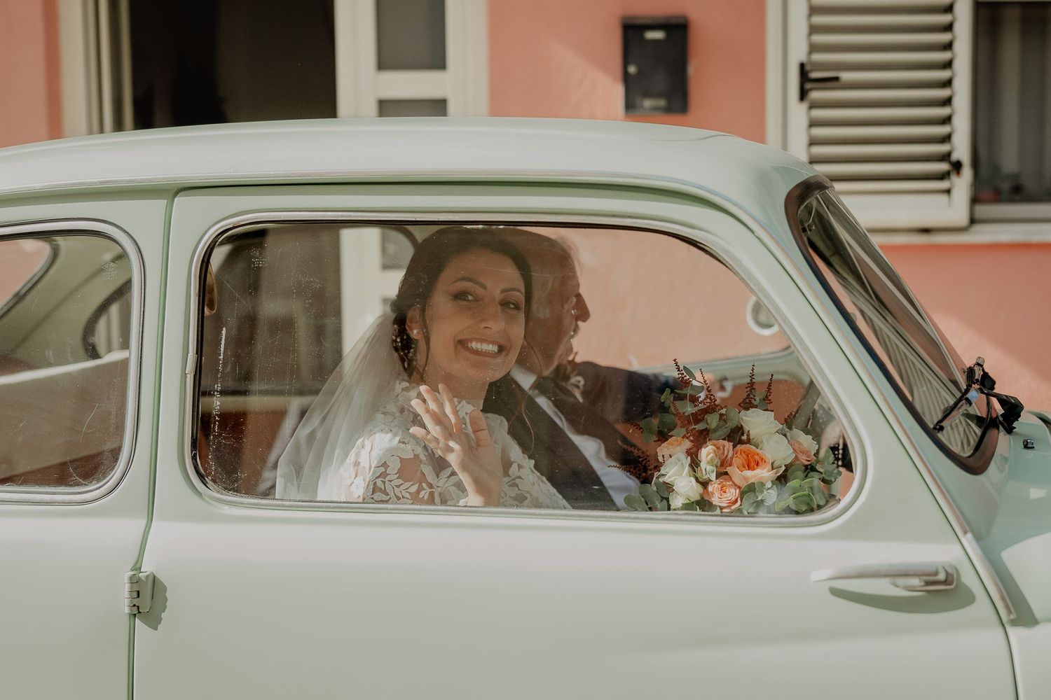 Maddalena sorride dal finestrino di una Fiat d’epoca.