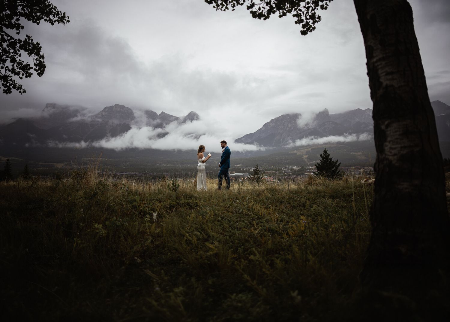 Mark and Jen reading private vows in a meadow overlooking Canmore and misty mountains