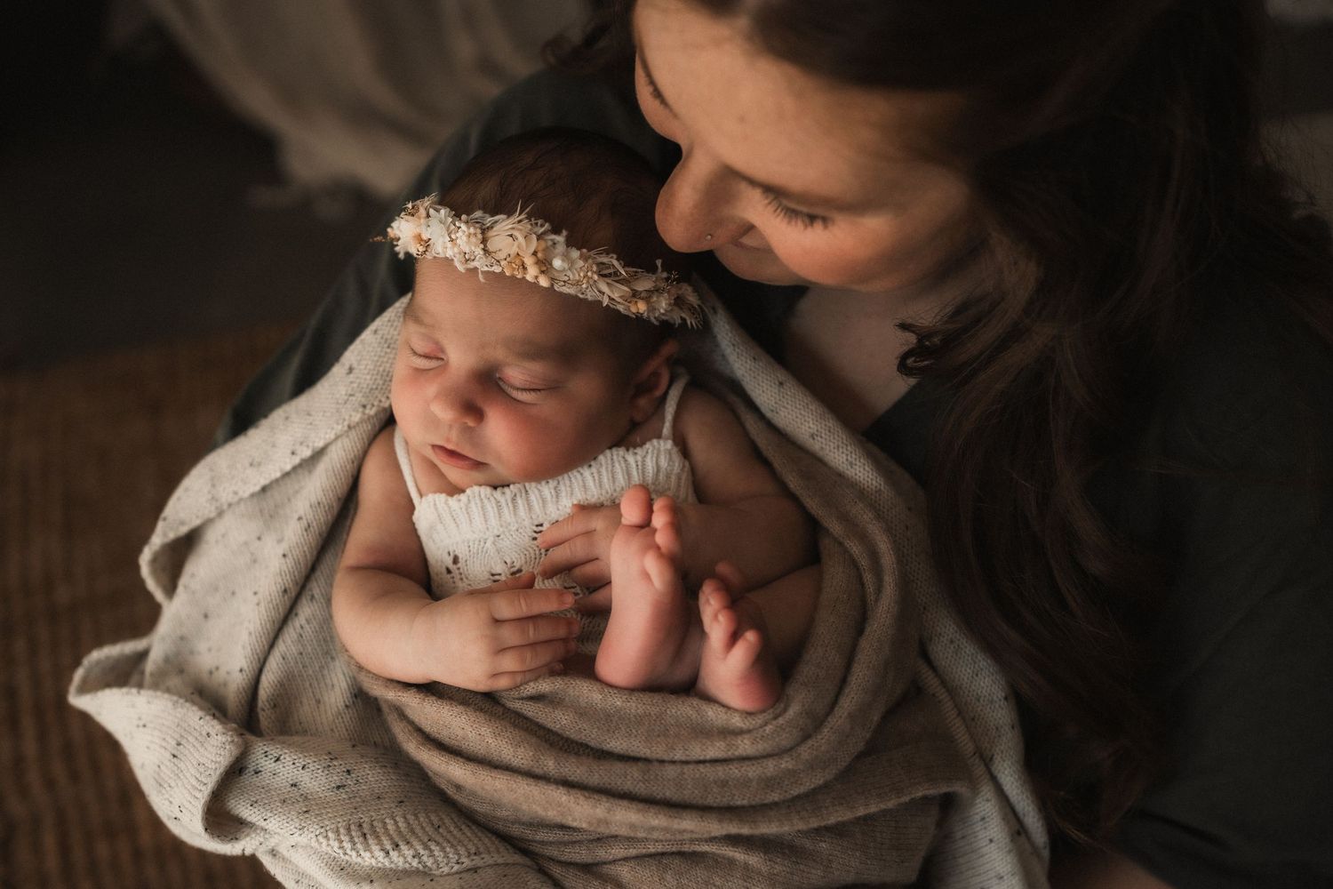 Gentle hands cradling sleeping newborn baby wrapped in soft white blanket.