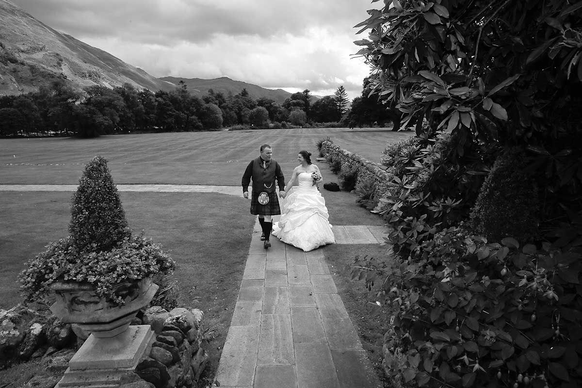 Black and white photo of a bride and groom walking down the path at Inn on the Lake - Glenridding