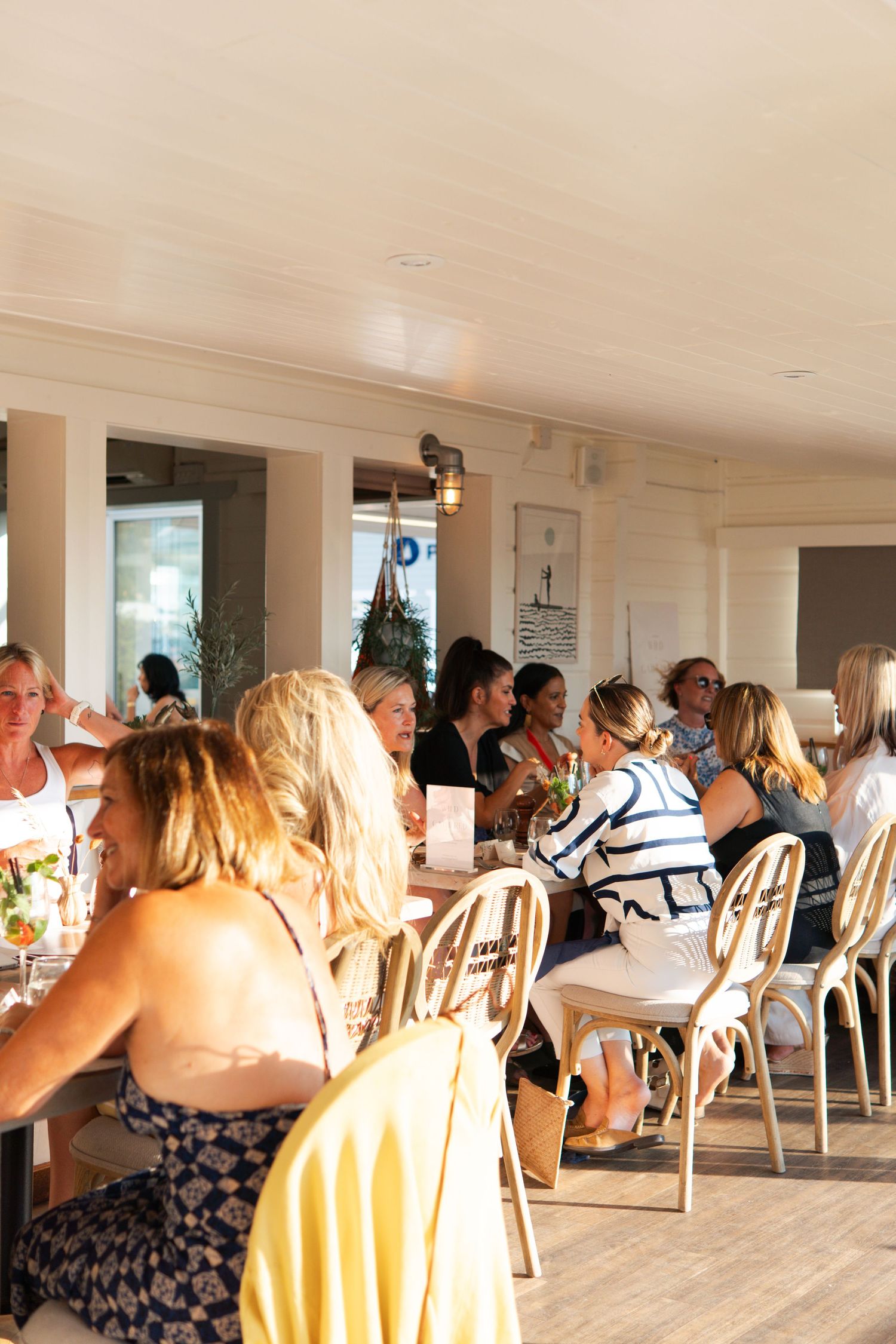 Groups of people dining together in a cozy restaurant with string lights and wooden beam ceiling decor.