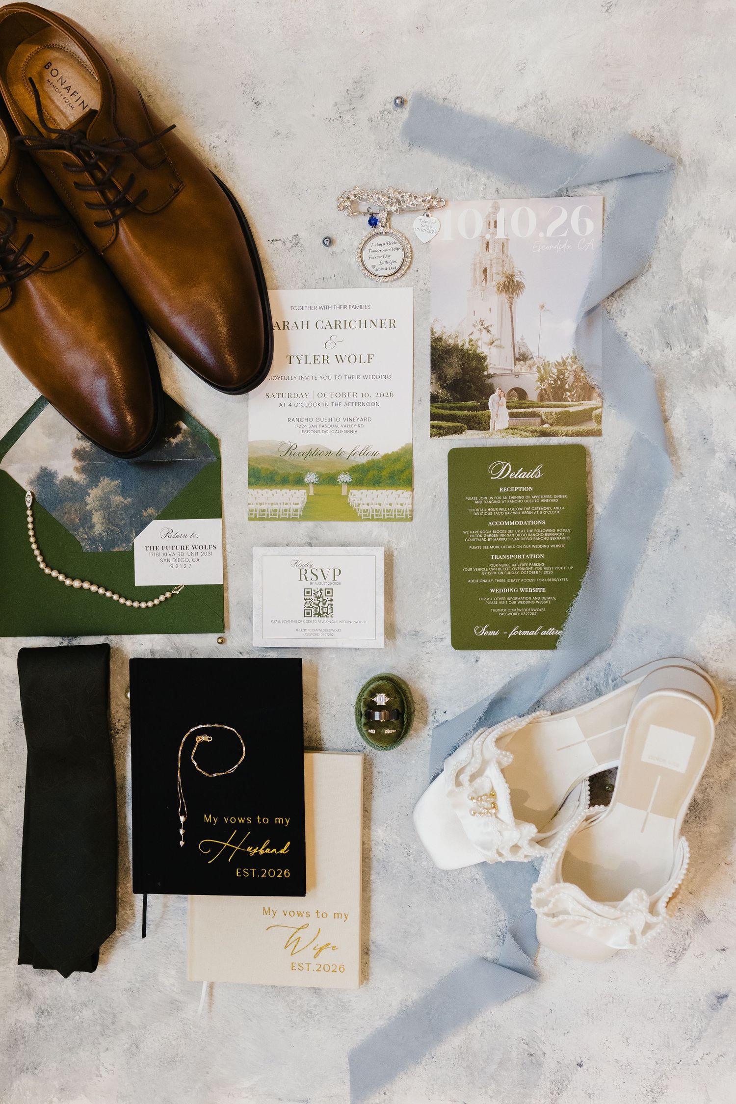 Wedding flat lay featuring brown leather shoes, invitation suite, vow books, green tie, white sandals and a blue silk ribbon.