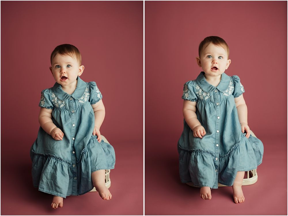 Adorable baby girl in teal dress sits on wooden stool against pink backdrop in professional studio portrait.
