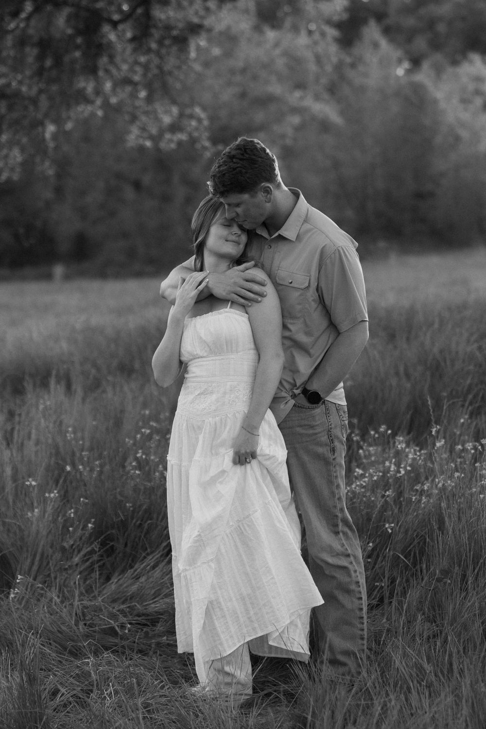 A black and white photo of a couple embracing one another in an open field.