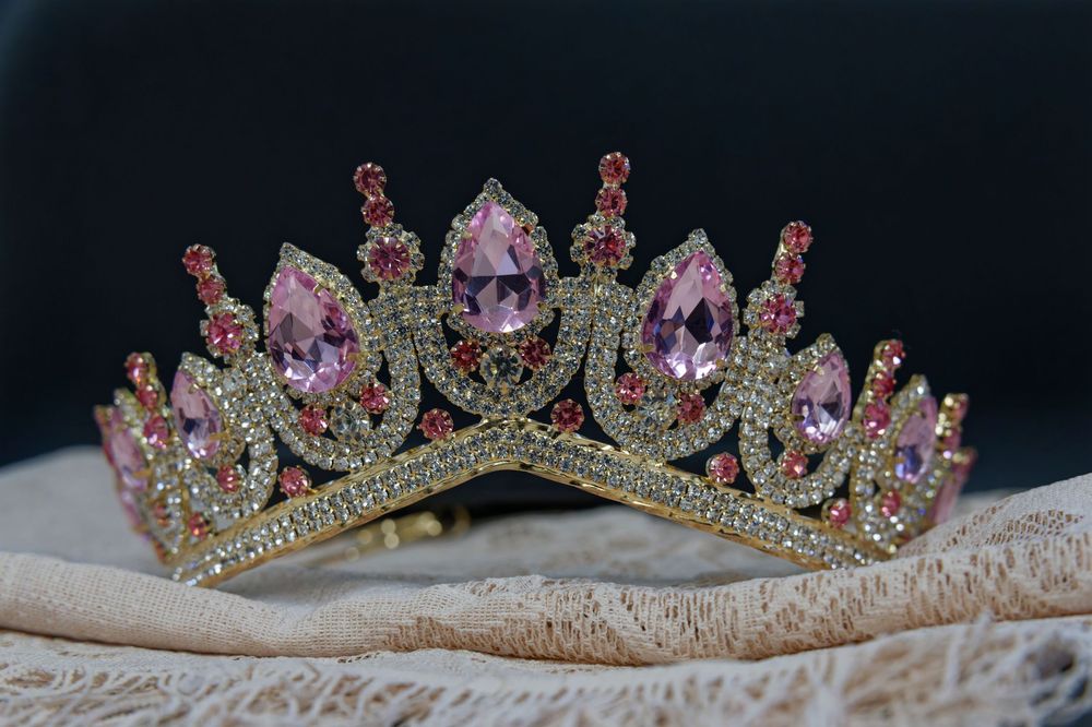 Elegant pink crystal and rhinestone tiara crown displayed on white fabric against dark background.