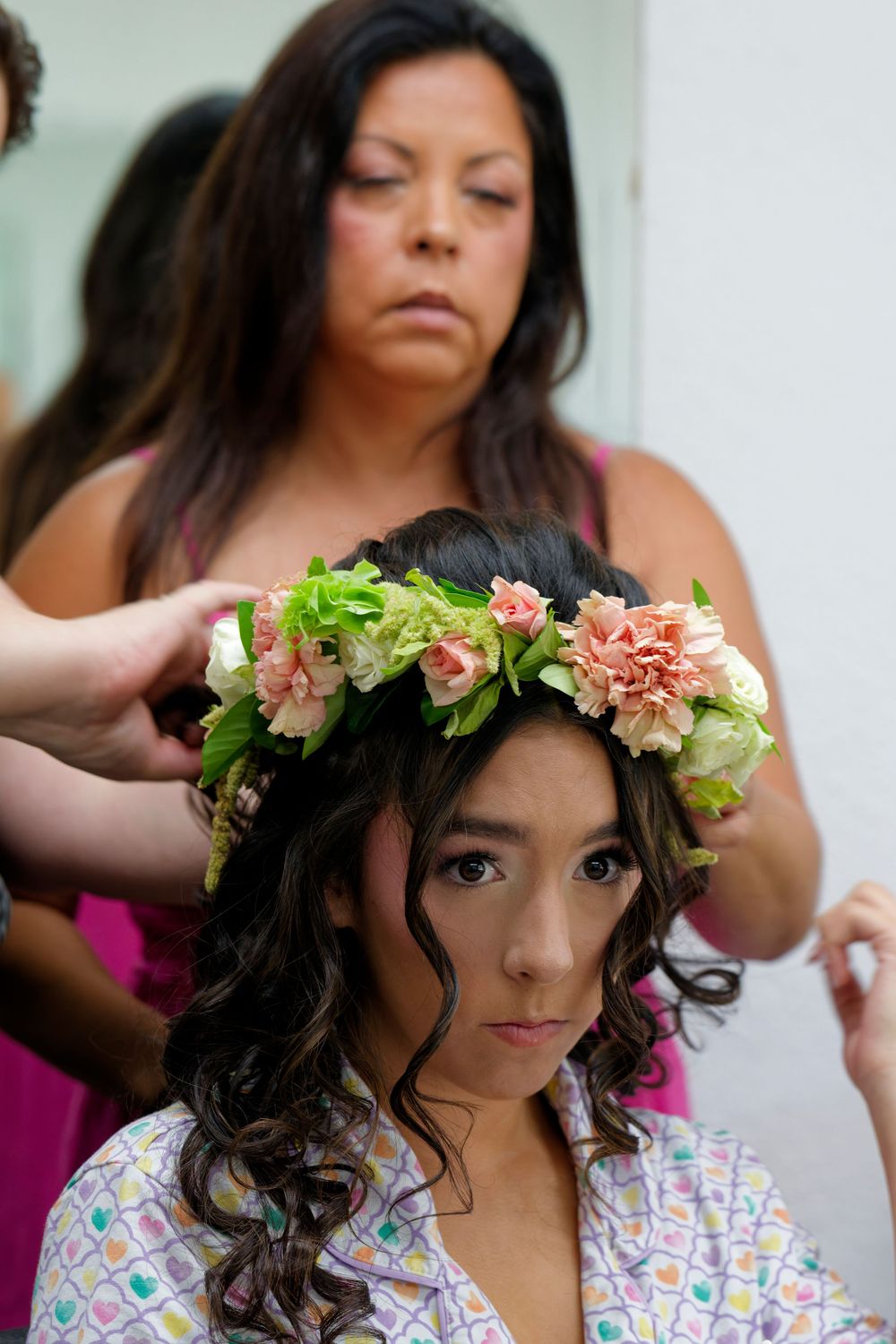 Stylist placing a floral crown on a young woman's hair before her quinceañera celebration.
