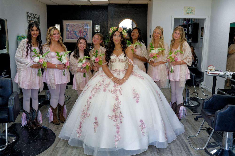 Quinceañera girl in white floral ball gown posing with her court of honor in a salon.