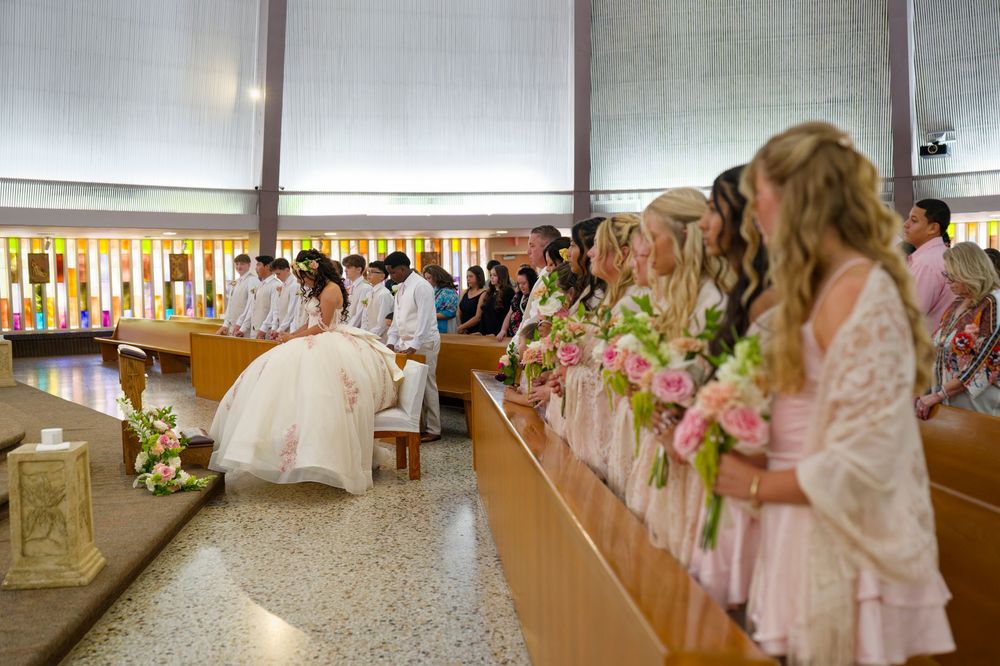 Quinceañera celebration in church with bridesmaids in pink dresses holding floral bouquets standing in pews.