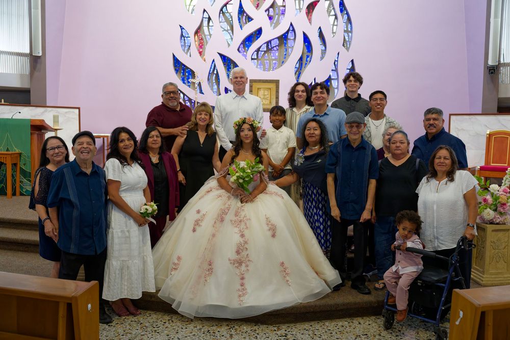 Family group photo at a quinceañera celebration inside a church with colorful stained glass windows.